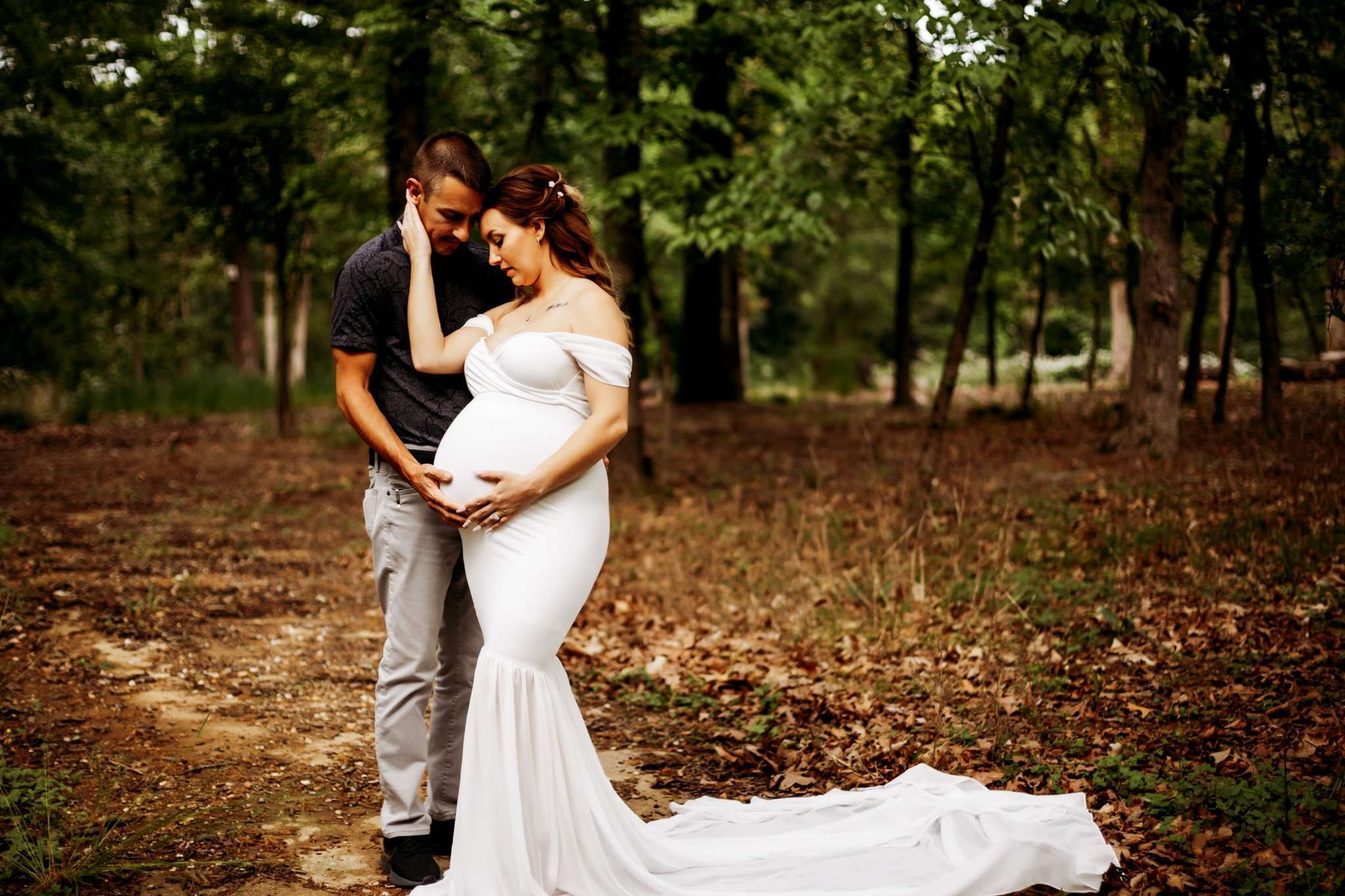 pregnant woman in white gown holding husbands face looking down at baby bump