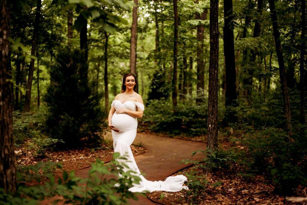 pregnant woman in white dress cradling her baby bump in a wooded area