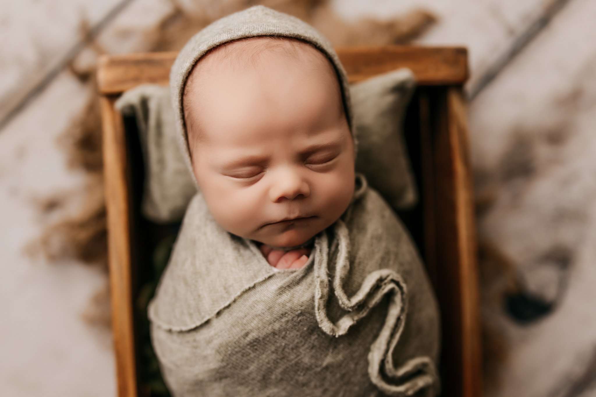 baby wrapped in green inside crate with matching bonnet on