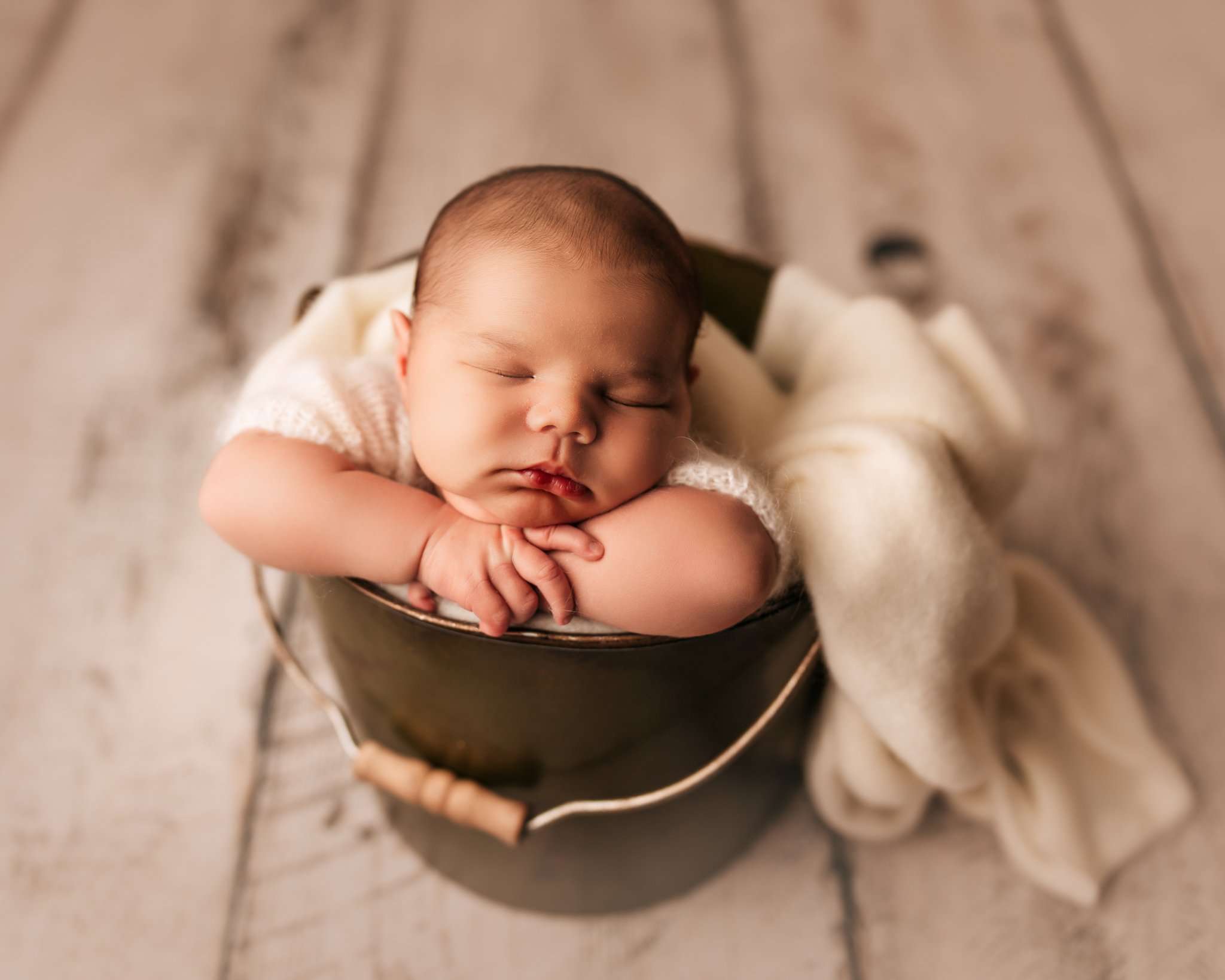 baby with head on hands inside bucket on white wood for newborn photography session