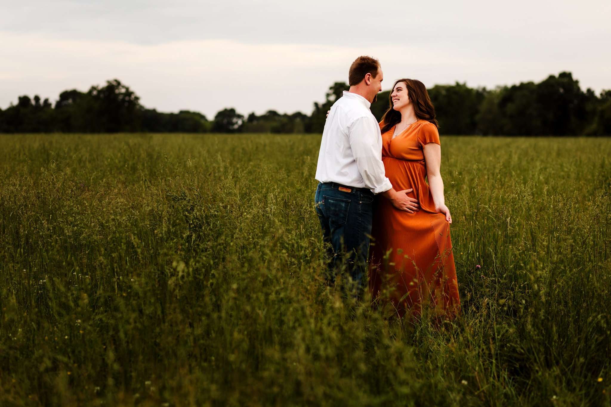 pregnant woman looking at her husband while holding maternity gown in overgrown field