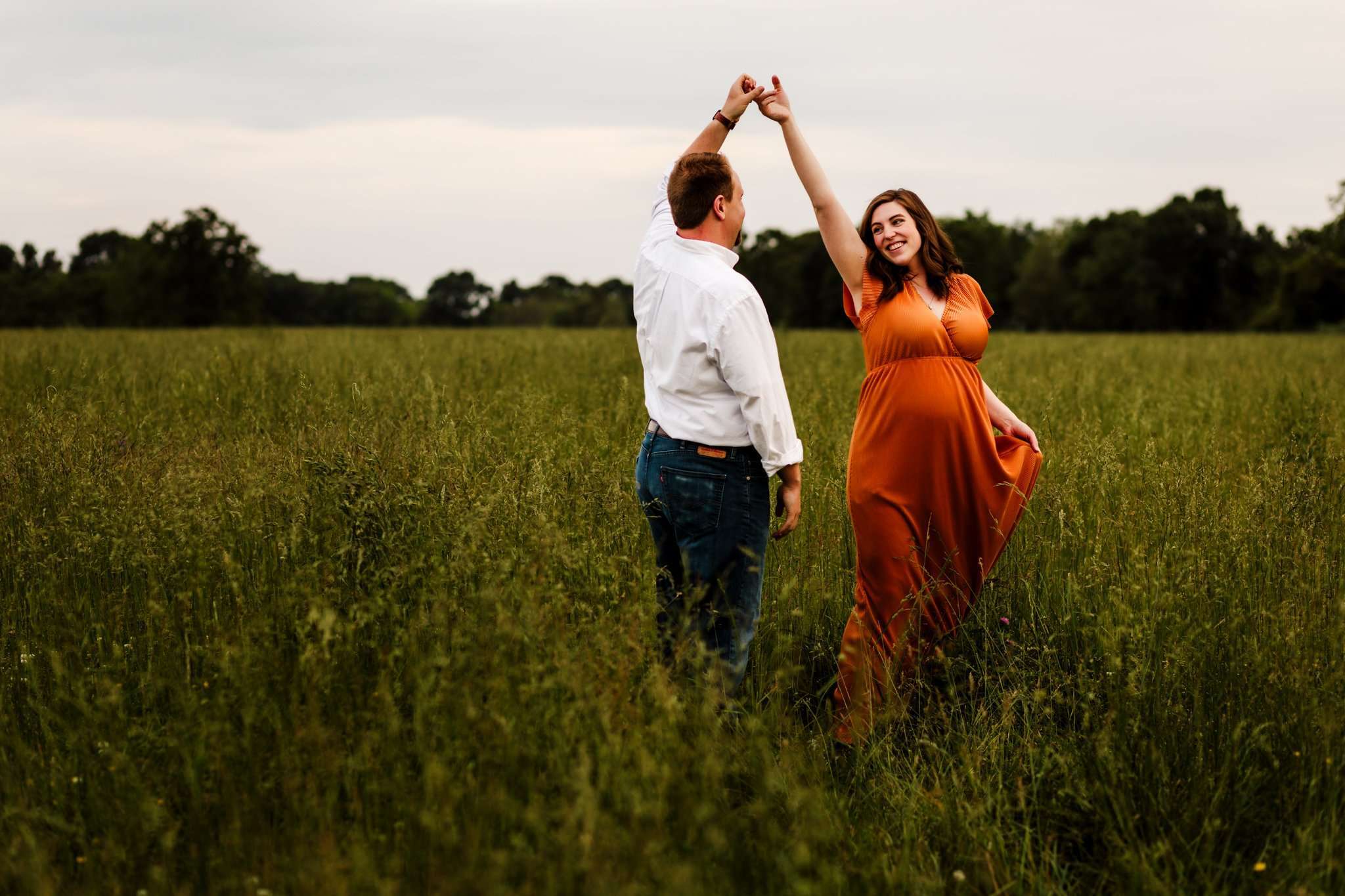 pregnant women dancing in orange dress with husband in overgrown field