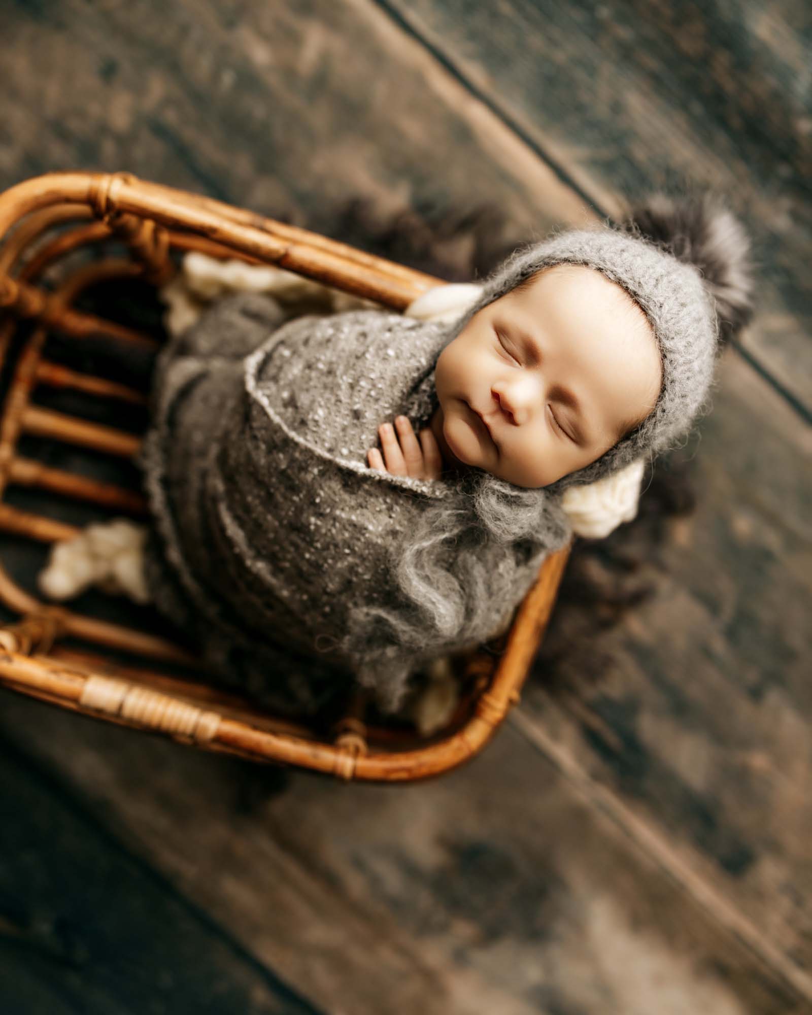 baby wrapped in dark gray inside basket with bonnet on
