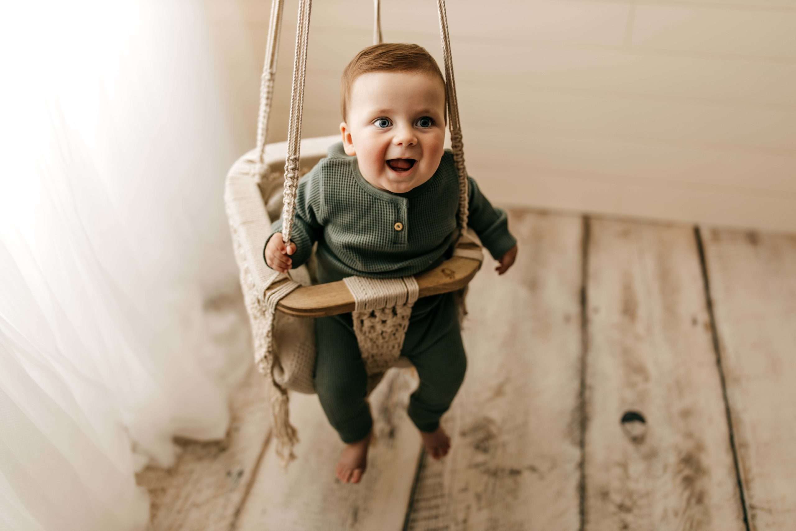 six month old in macrame swing smiling by window