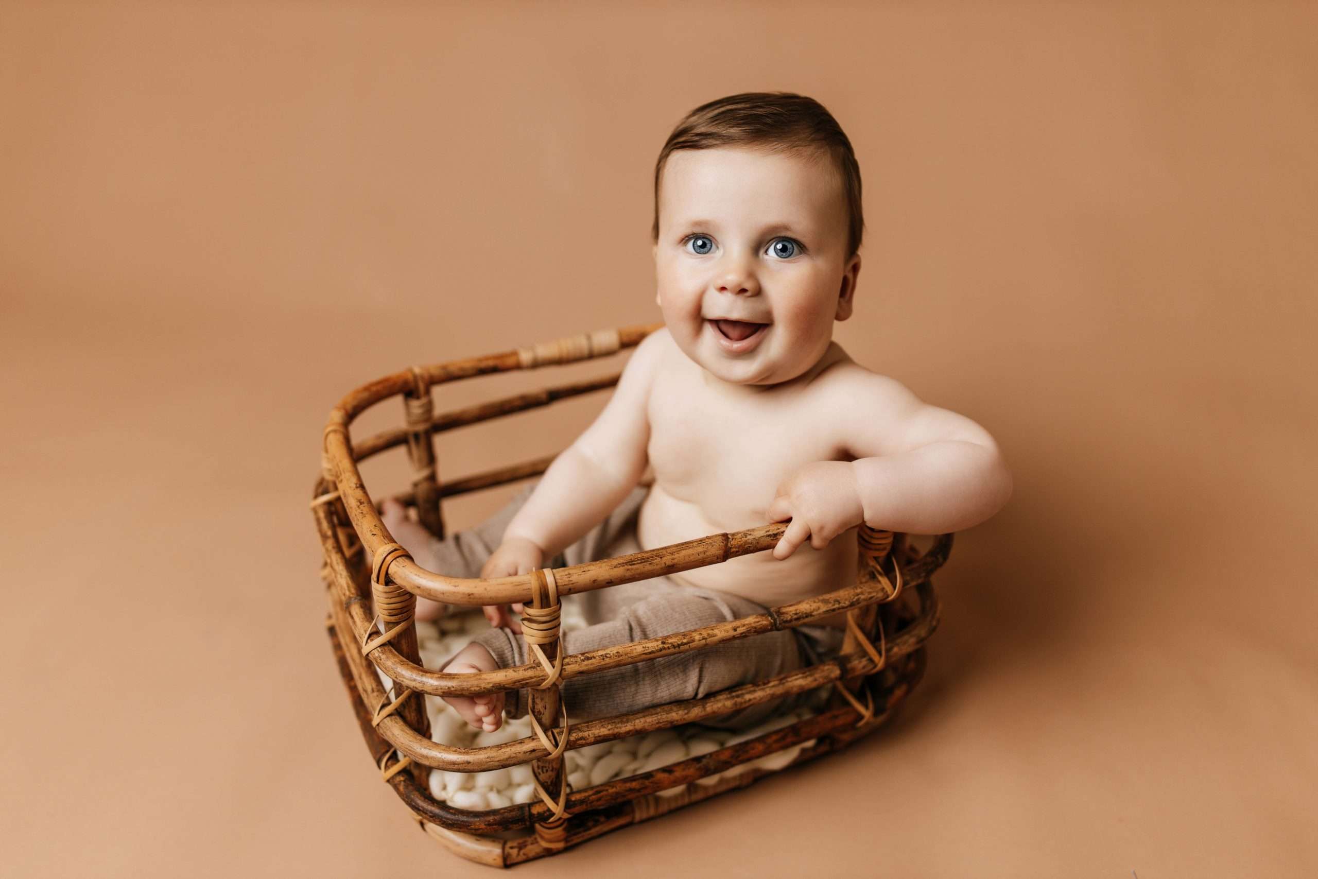 six month old sitting in bamboo basket on tan backdrop