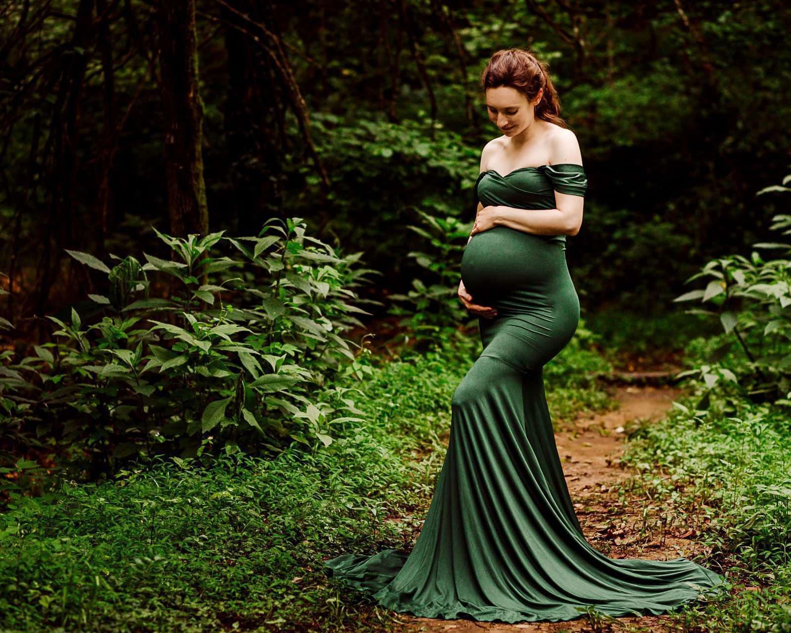 pregnant woman standing in wooded area while cradling her baby belly