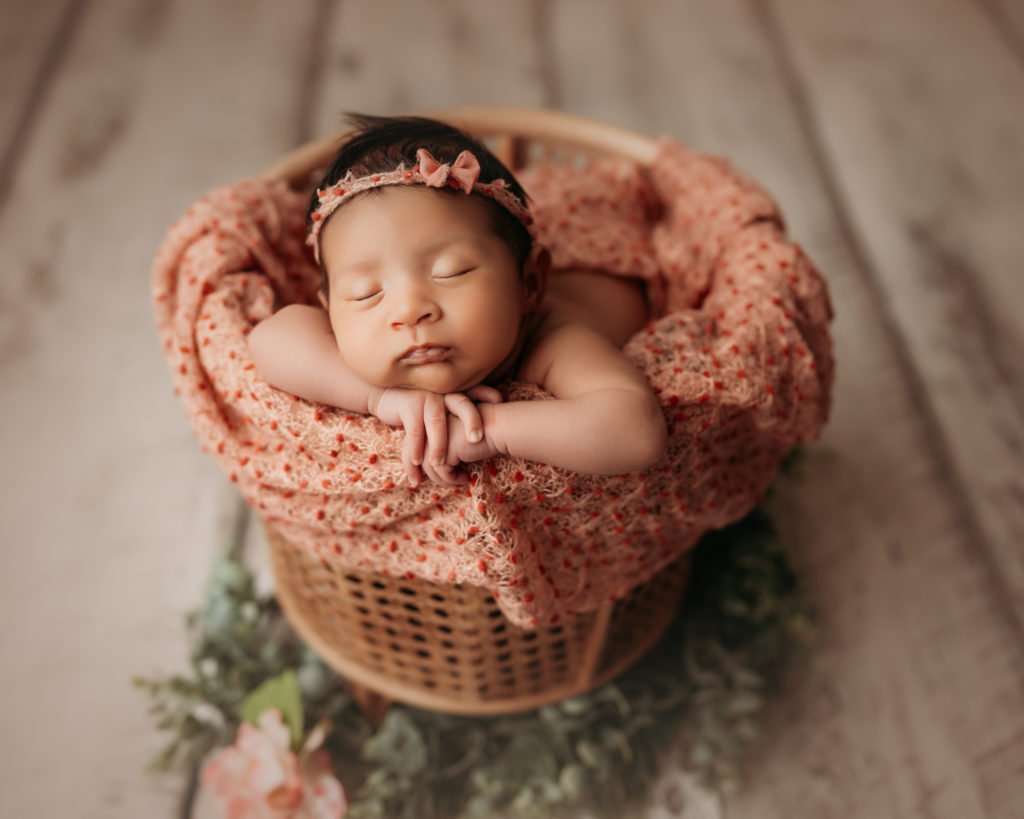 newborn on white wood floor posed in a bamboo basket during newborn photography session