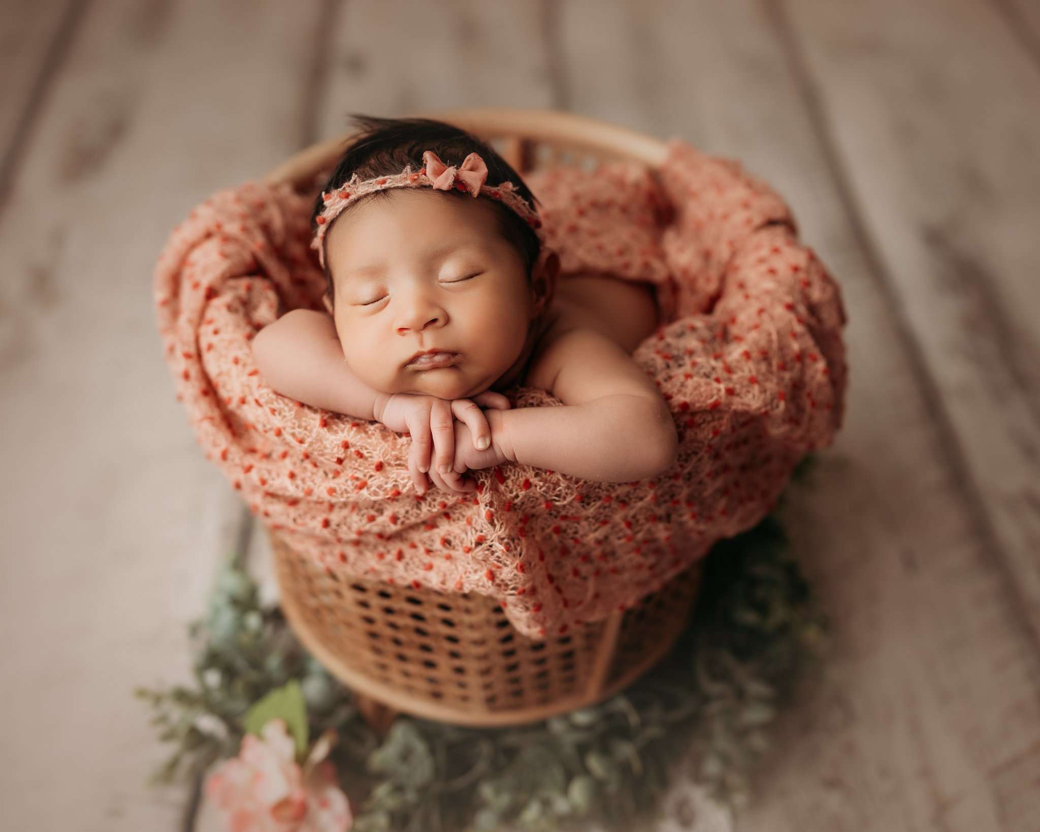 newborn on white wood floor posed in a bamboo basket