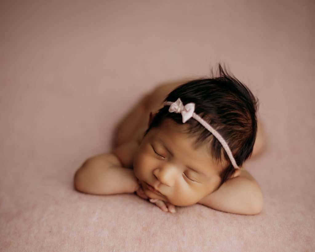 newborn on pink backdrop with head resting on hands during newborn photography session