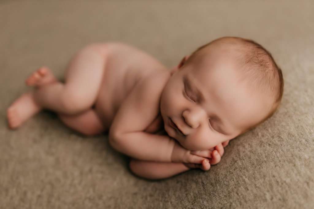 baby on light green backdrop in sleeping pose with hands by head