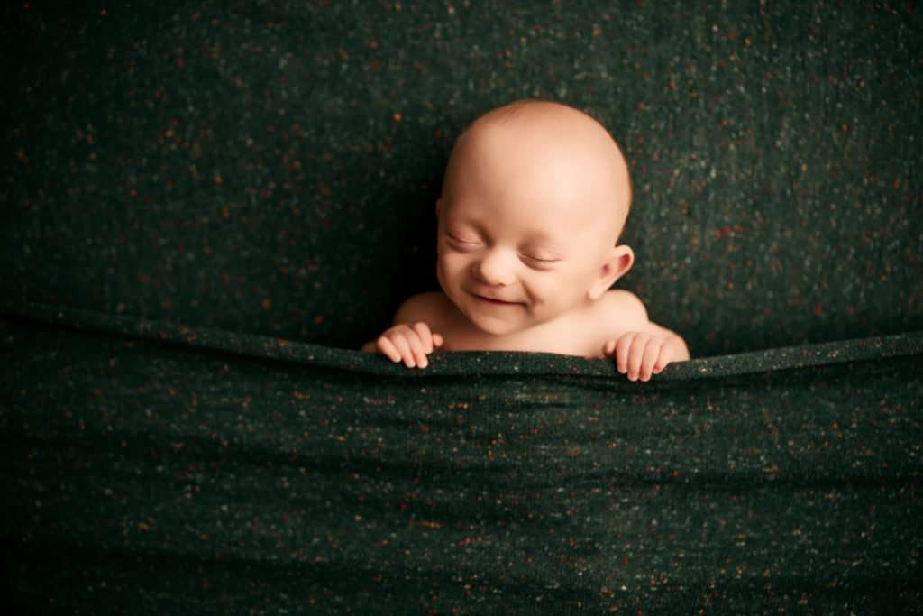 baby laying on back smiling on a green backdrop