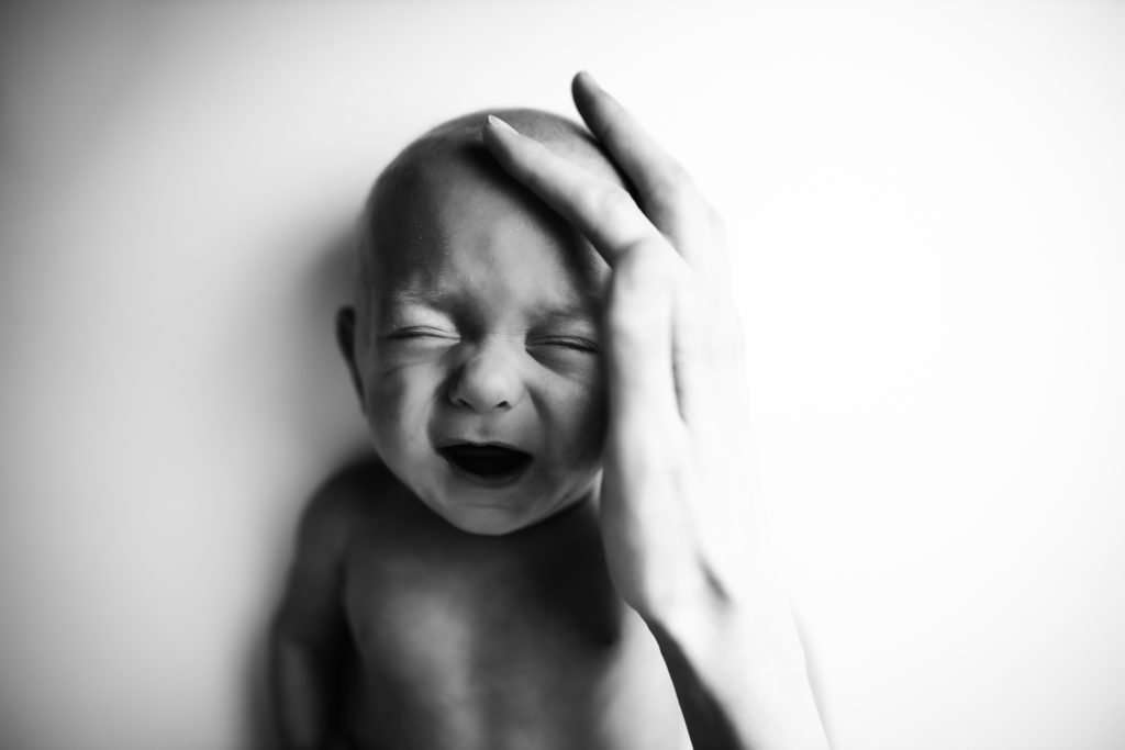 baby on white backdrop with moms hand comforting him