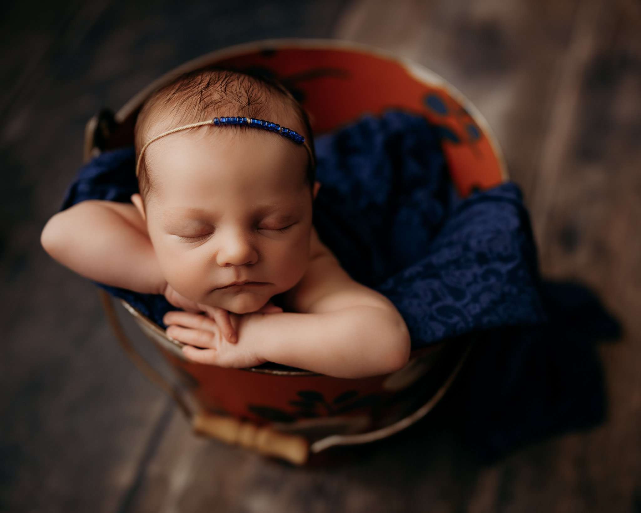 baby in bucket pose on dark wood floor with bucket being orange and navy floral