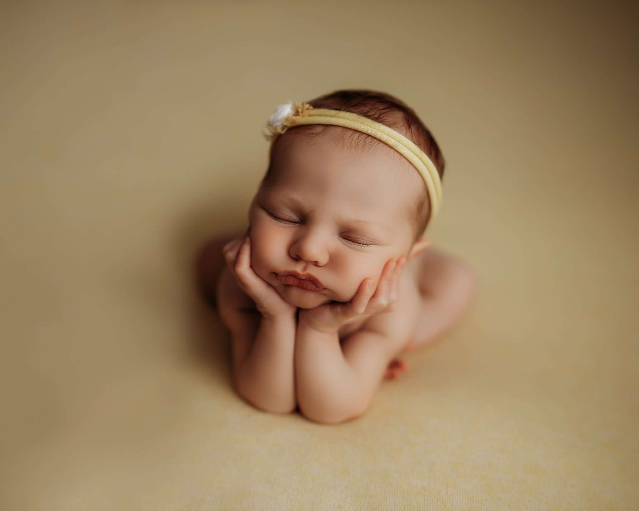 newborn in frog pose on yellow backdrop