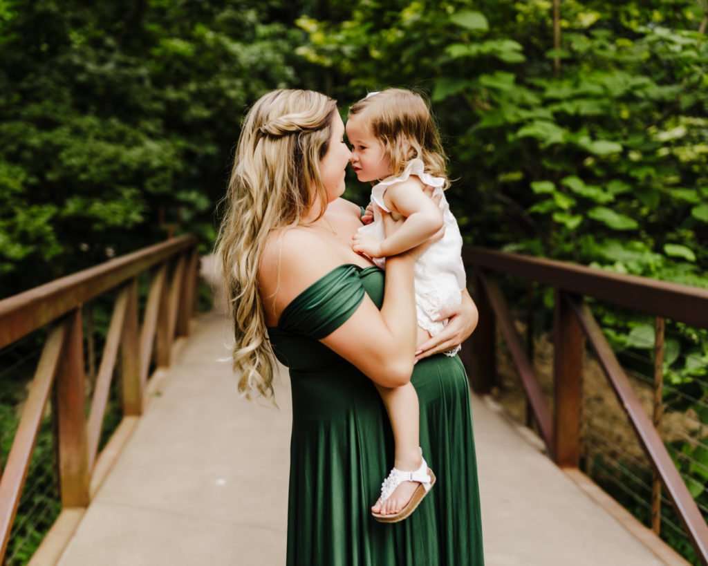 mom and daughter snuggling together during maternity session with foliage around them.