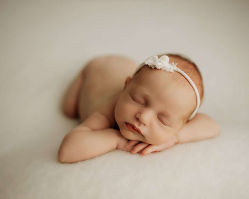 newborn baby on cream backdrop sleeping with her head on her hands