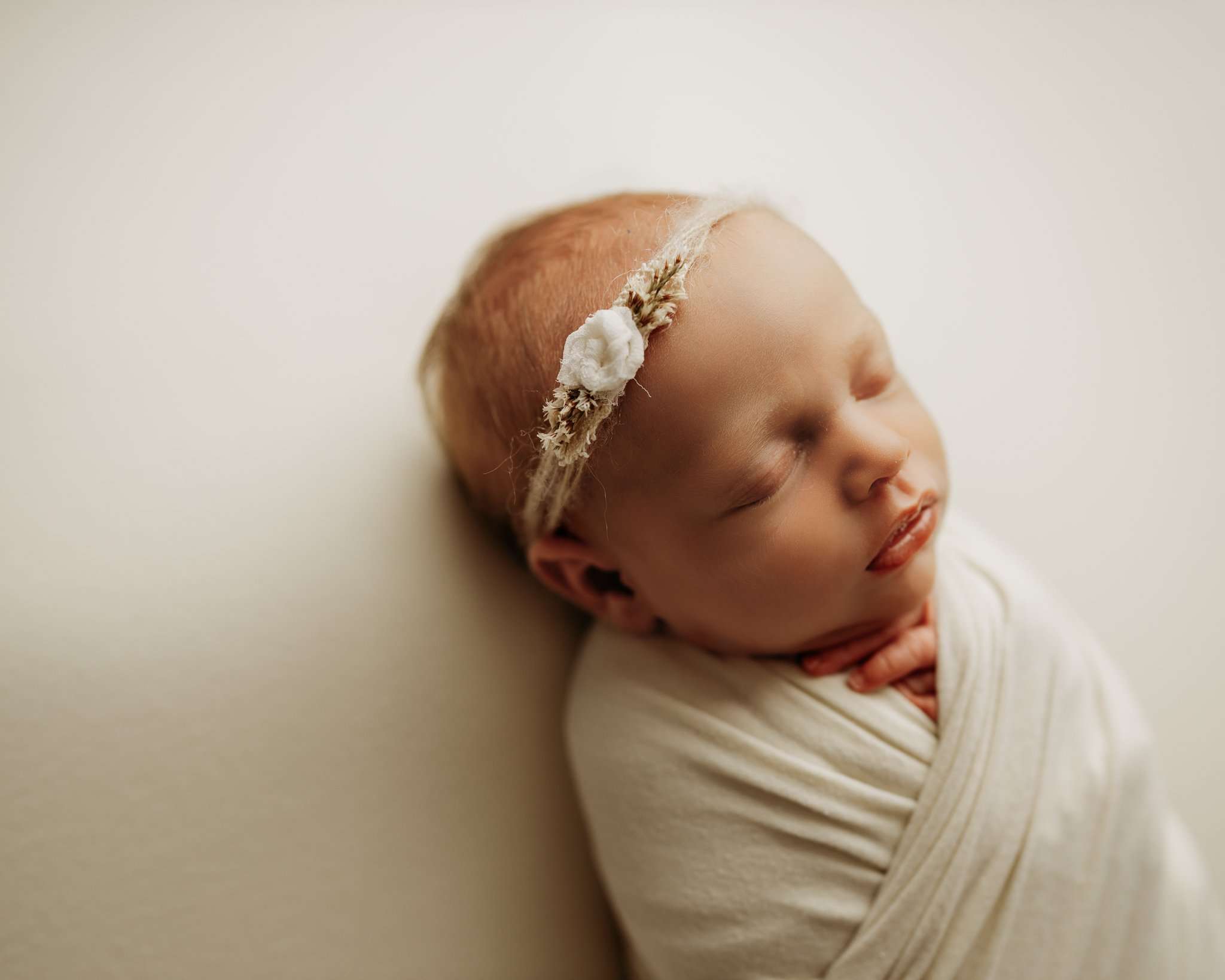 newborn on cream backdrop while wrapped and sleeping
