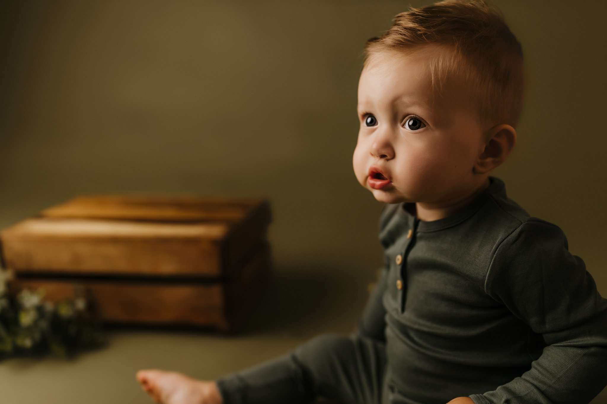 one year old sitting on olive green backdrop while staring at the movie playing in the studio