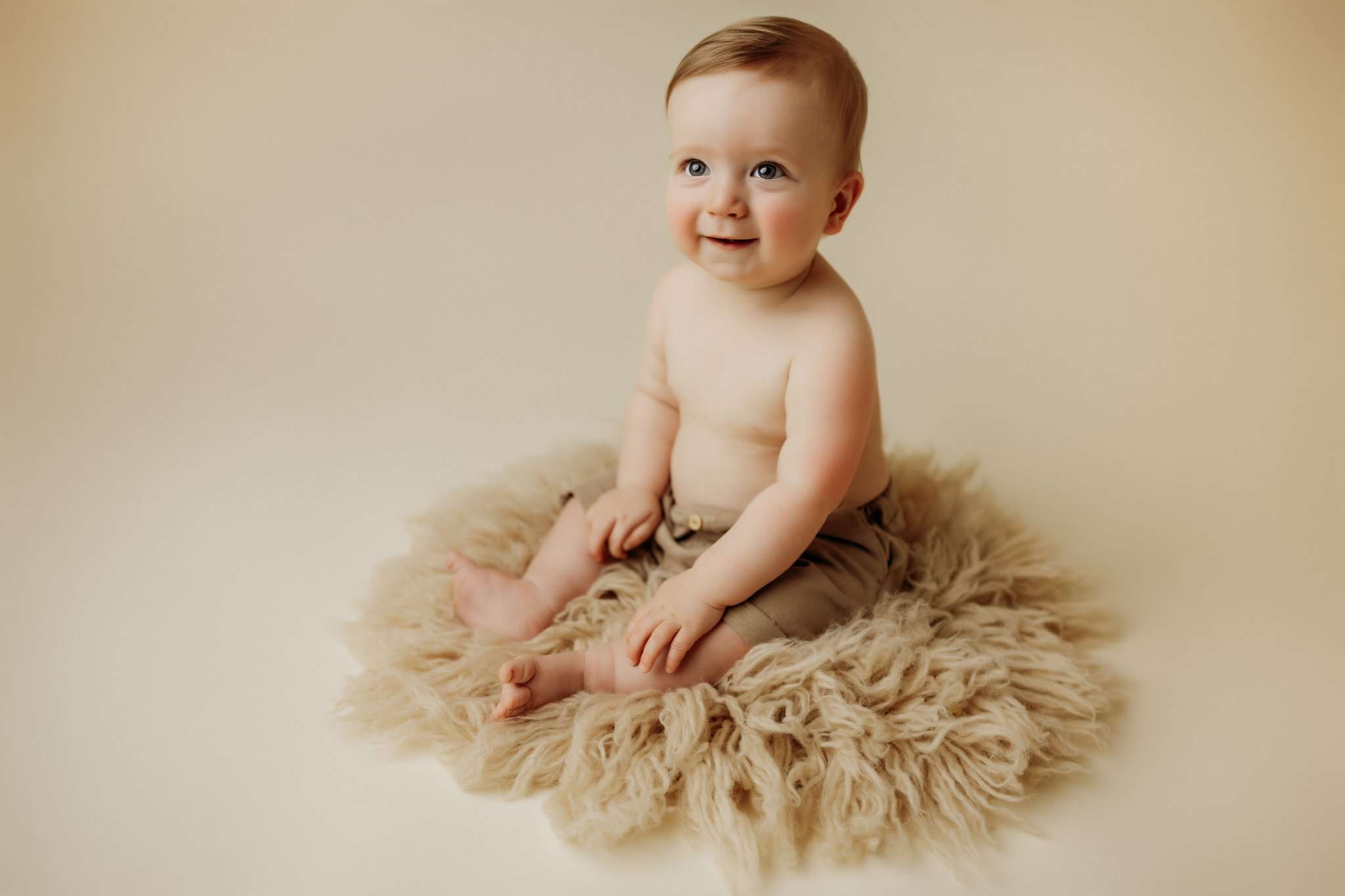 nwa childrens session with baby boy on tan flokati round rug and shorts while smiling