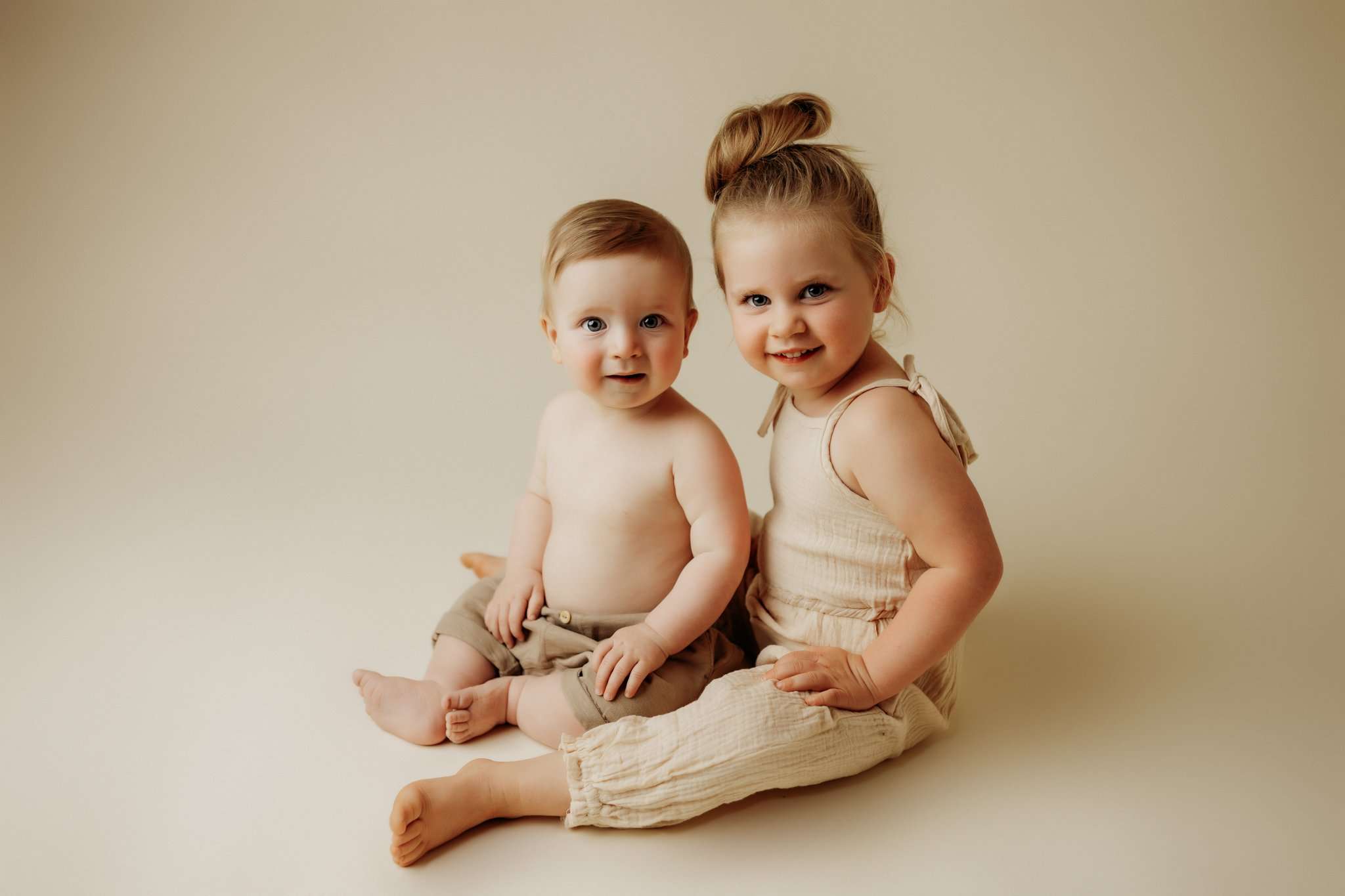 siblings posed next to eachother smiling at camera on cream backdrop
