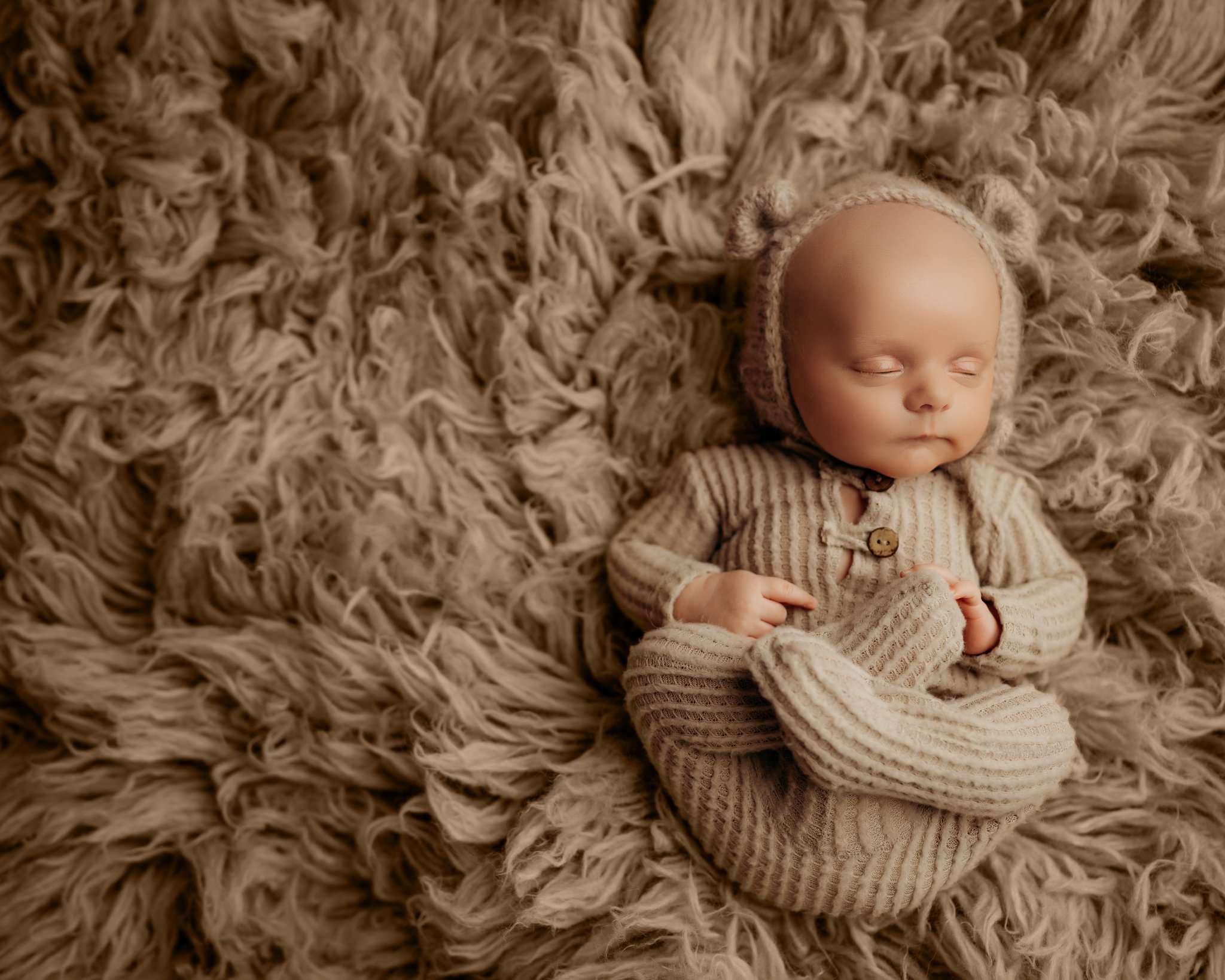 baby on light brown flokati rug with feet up and bear bonnet sleeping
