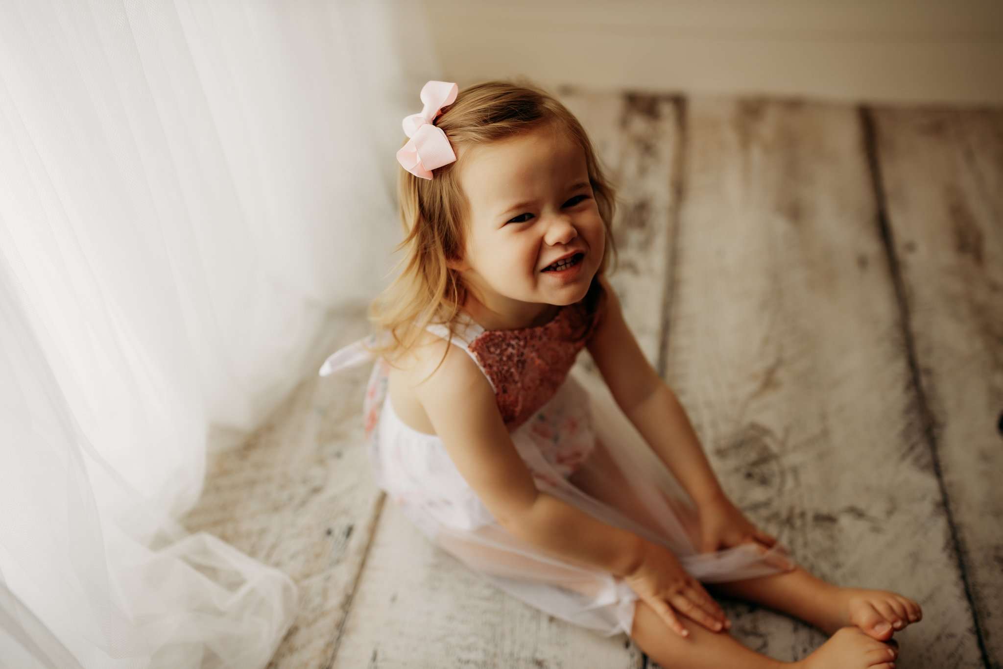 nwa childrens photography in studio with child sitting on wood background while smiling at the camera next to the faux window.
