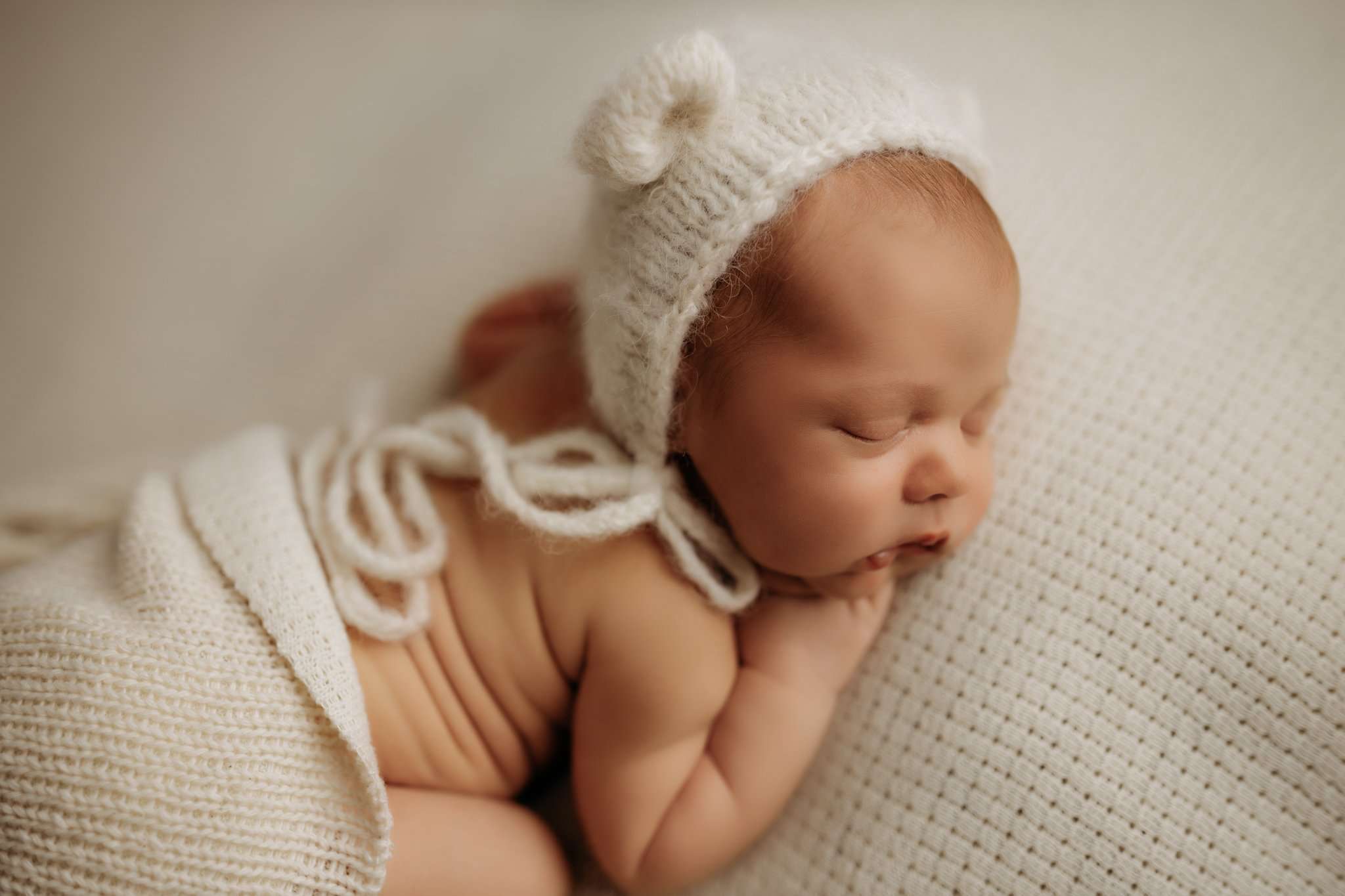 NWA newborn on a white backdrop wearing a bear bonnet and sleeping