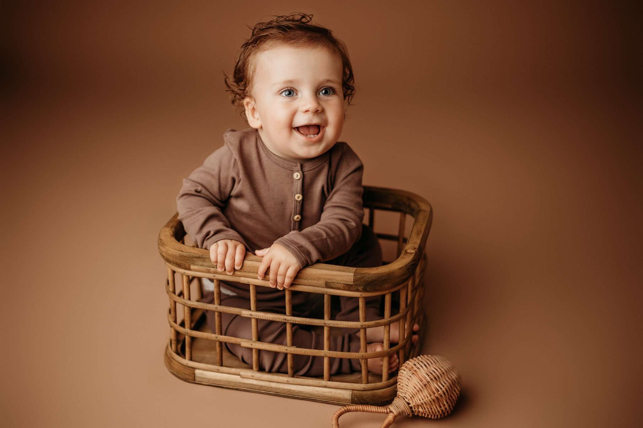 NWA one year little boy in studio on brown backdrop in crate smiling at the camera