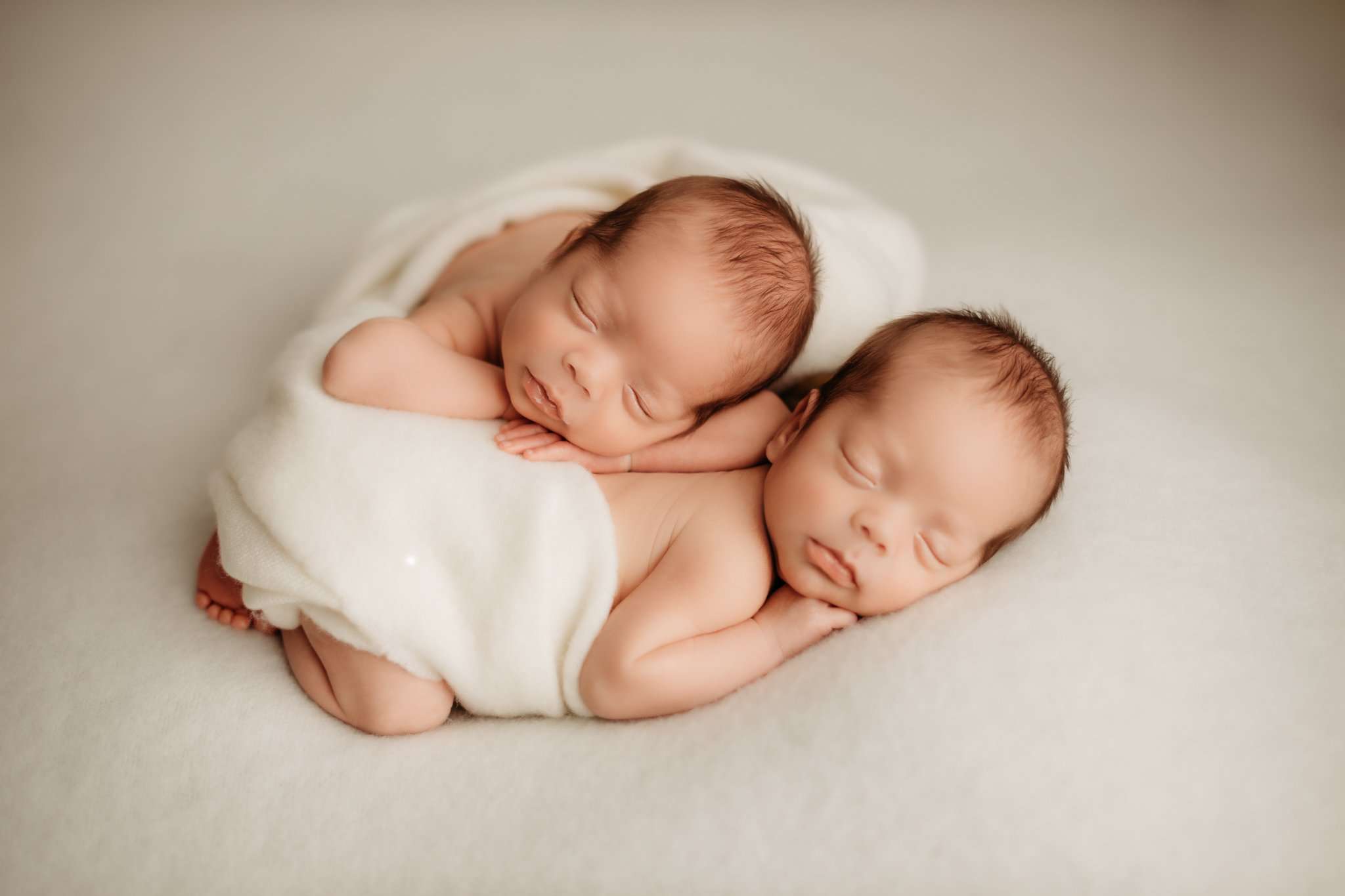 twin photography session with one twin on the others back on a white background and the twins sleeping