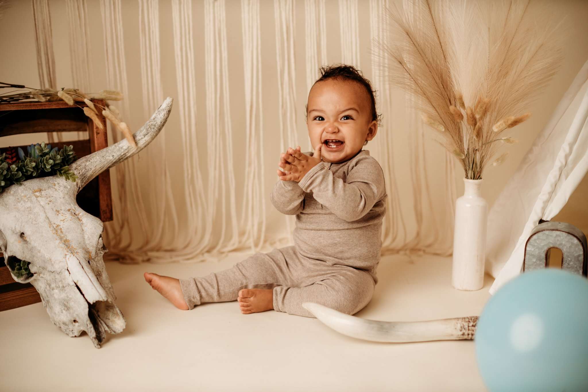 baby boy sitting on a neutral backdrop smiling at the camera and clapping his hands