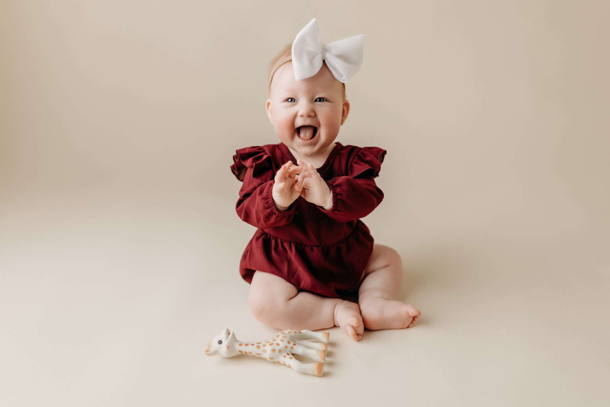 NWA milestone photography happy girl clapping for pictures 6 month old on a cream backdrop sitting with a burgandy romper on while smiling and clapping