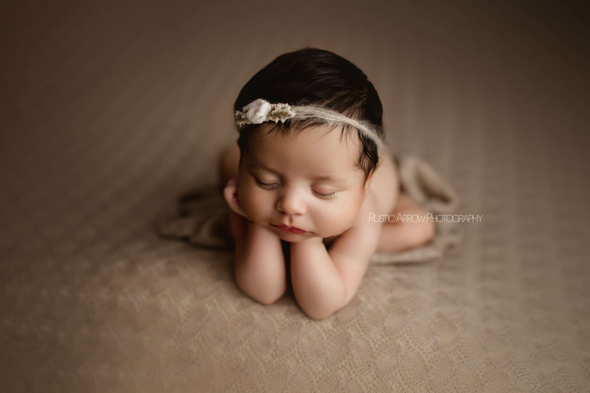 baby in frog pose in studio in northwest arkansas on a tan backdrop