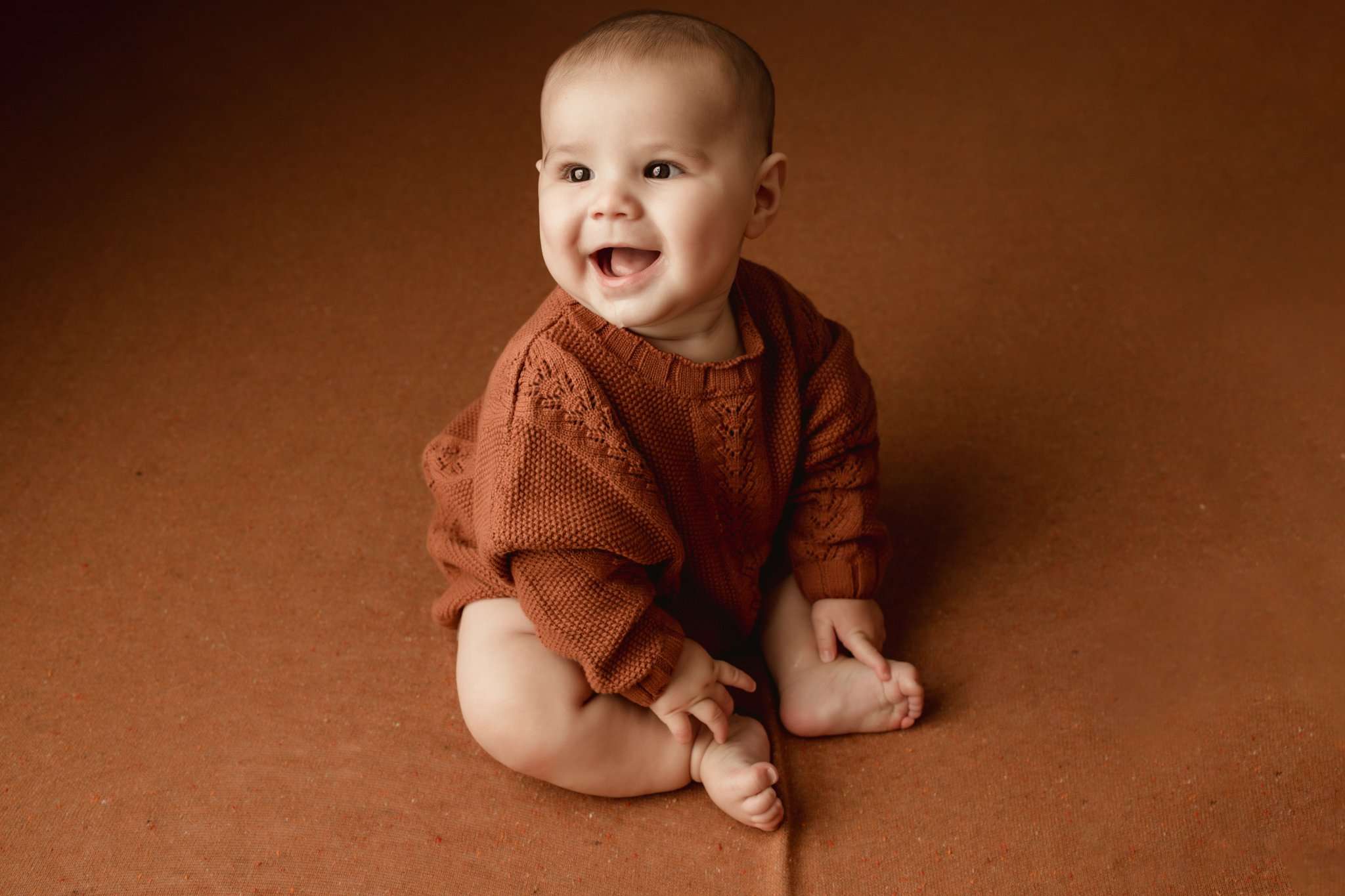 toddler sitting on an orange background wearing an orange sweater smiling