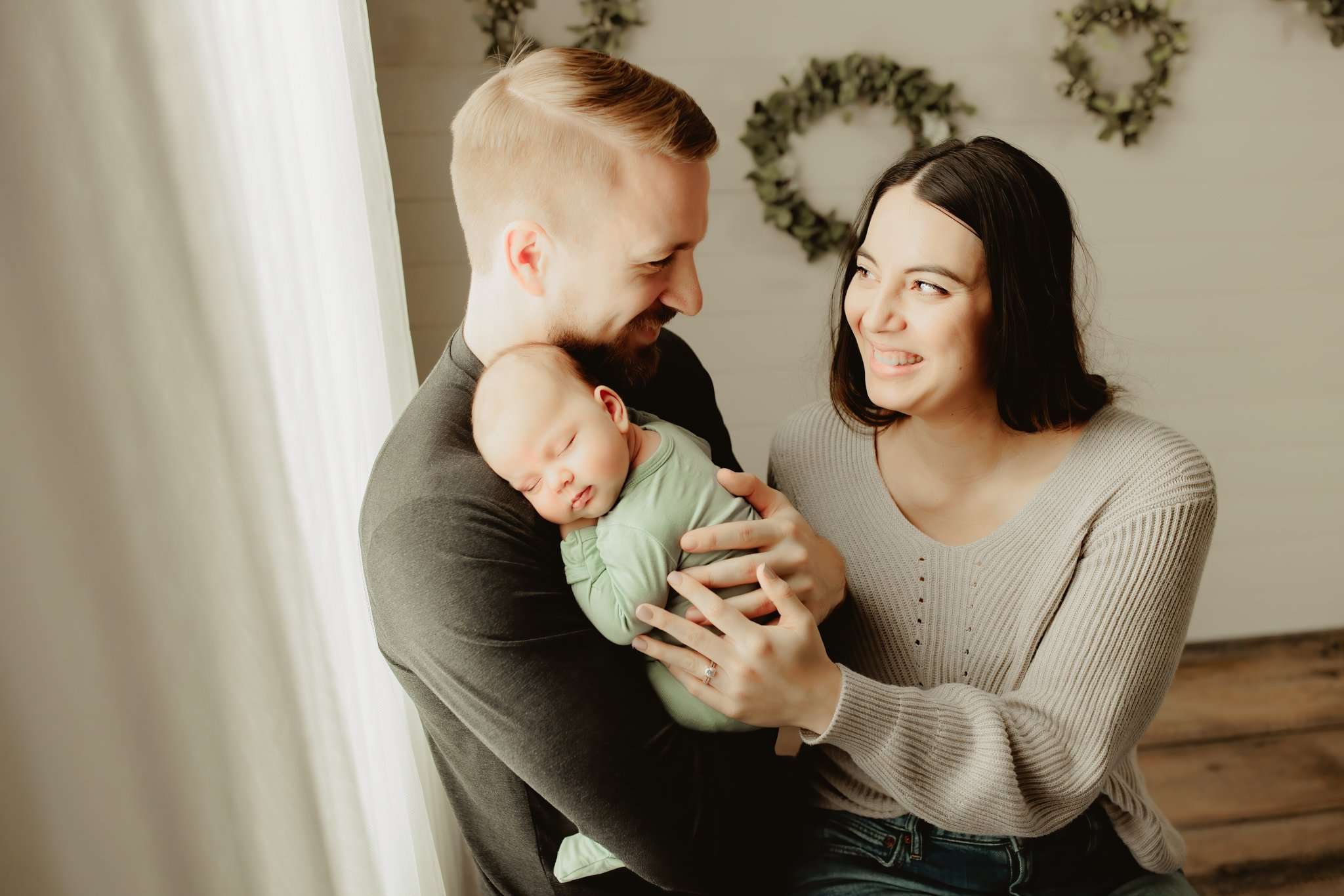 family holding their newborn next to an open window while the parents look at eachother and smile