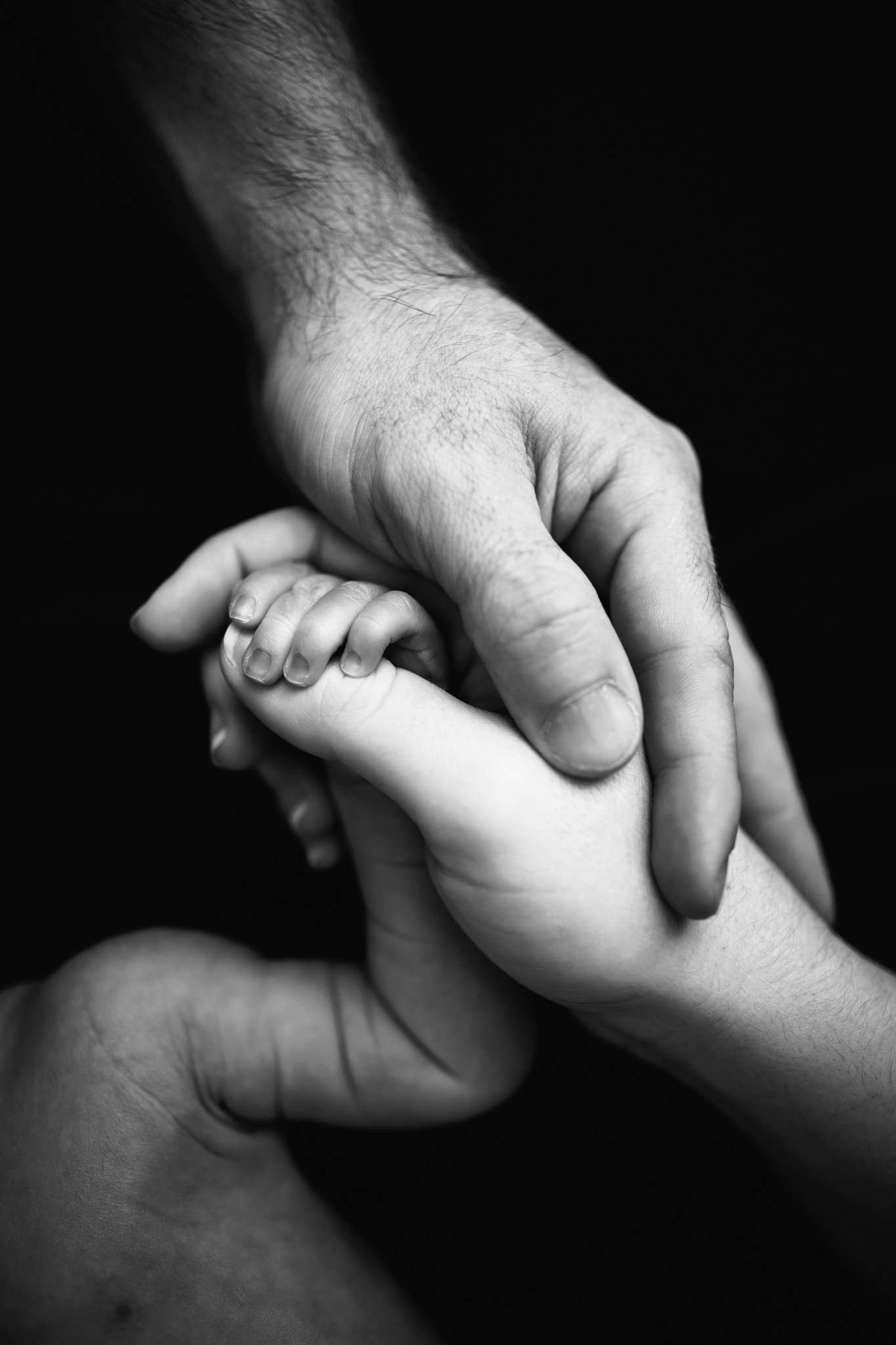 close up image of parents hands with child in black and white