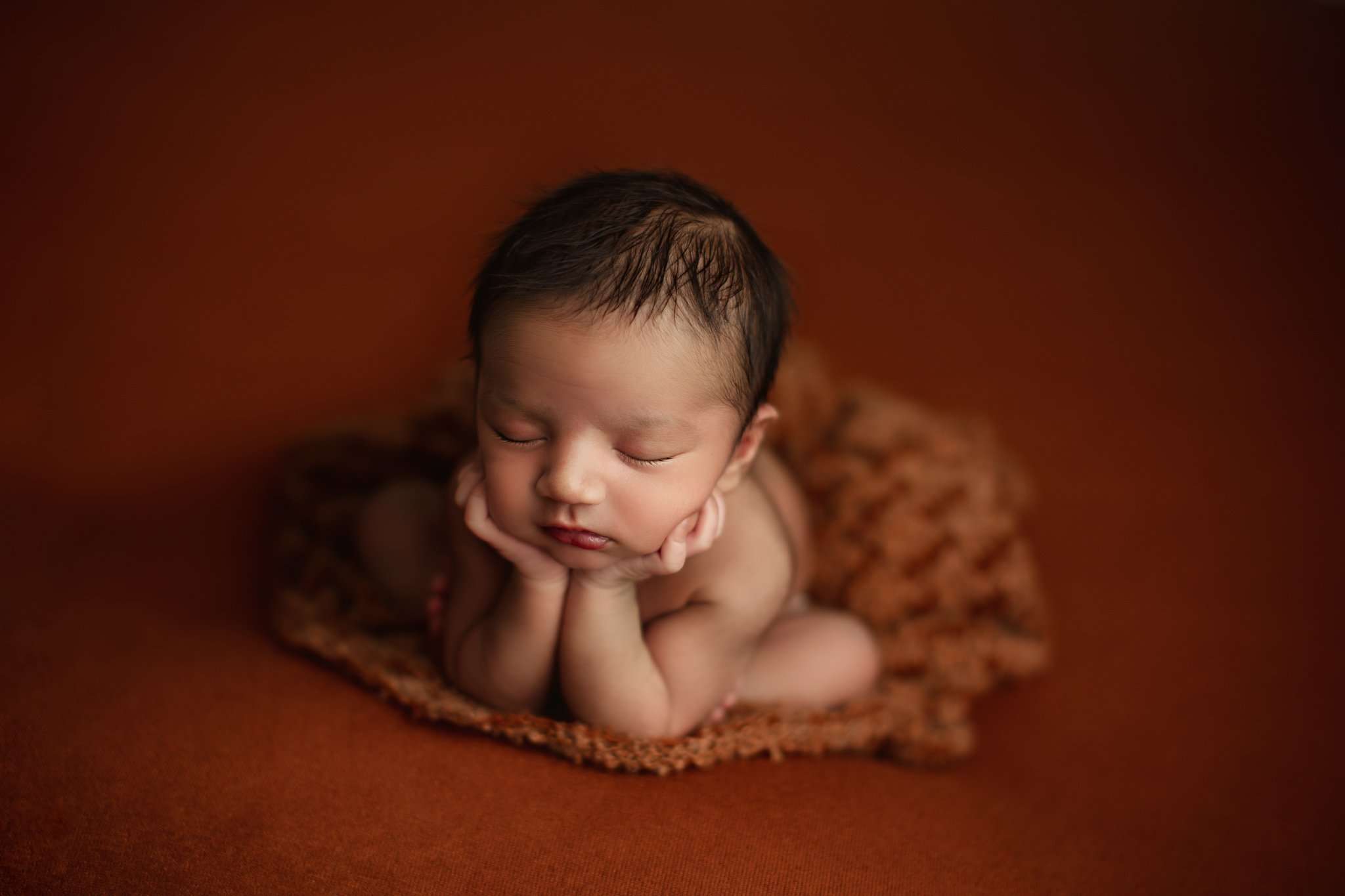 newborn baby in frog pose on an orange backdrop