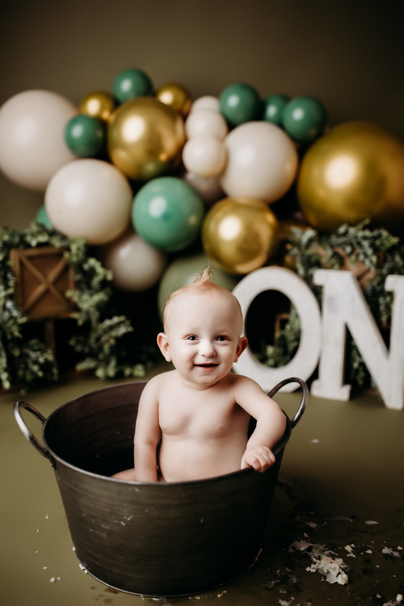 one year old in studio smiling at the camera in a tin bath