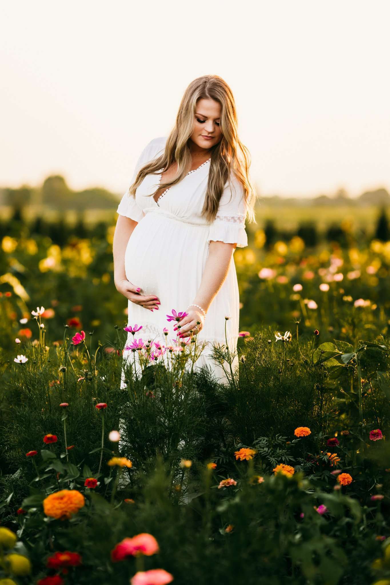 pregnant woman in a wildflower patch wearing a white dress