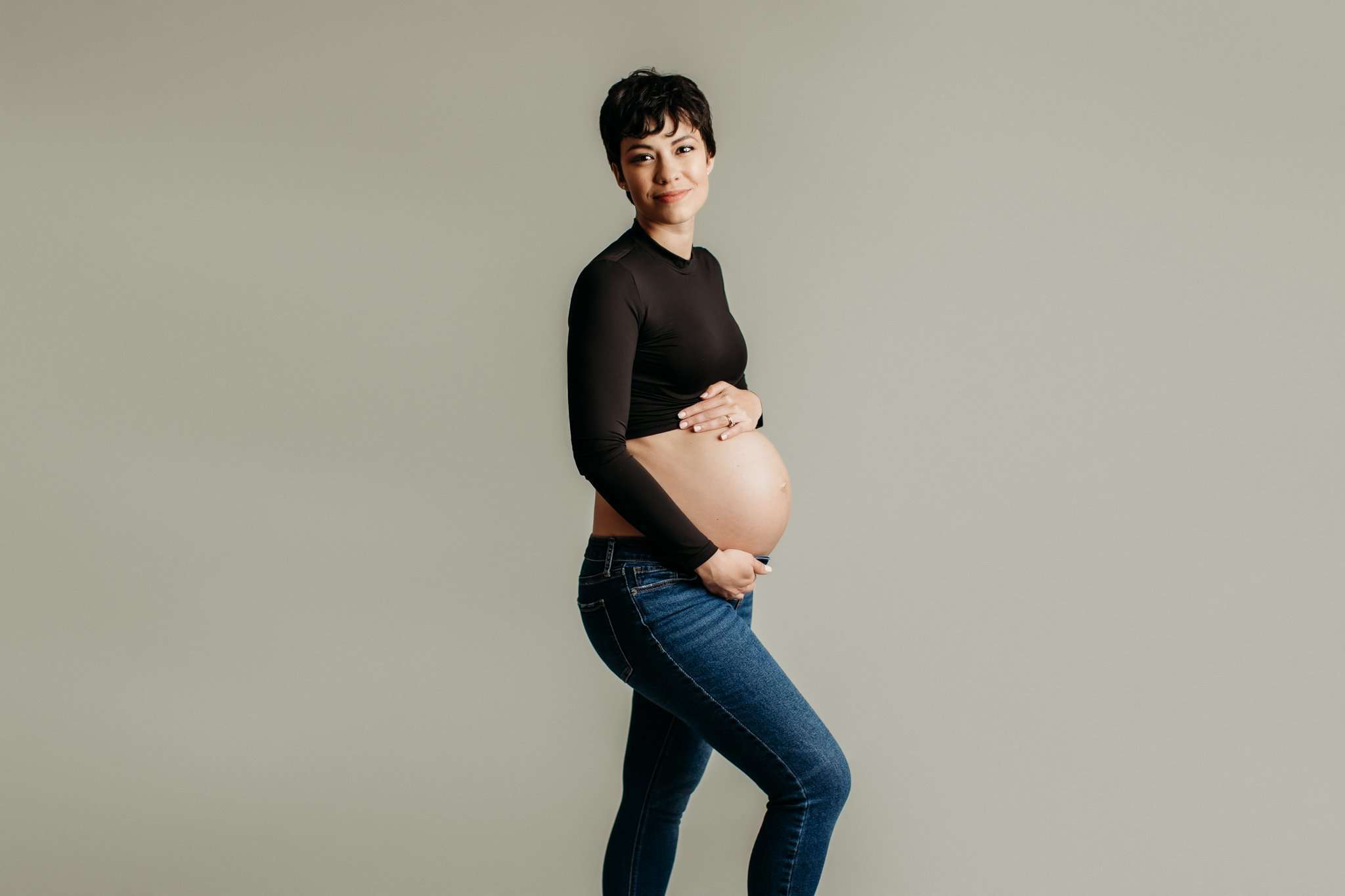 mom in a black crop top and jeans looking down at her belly